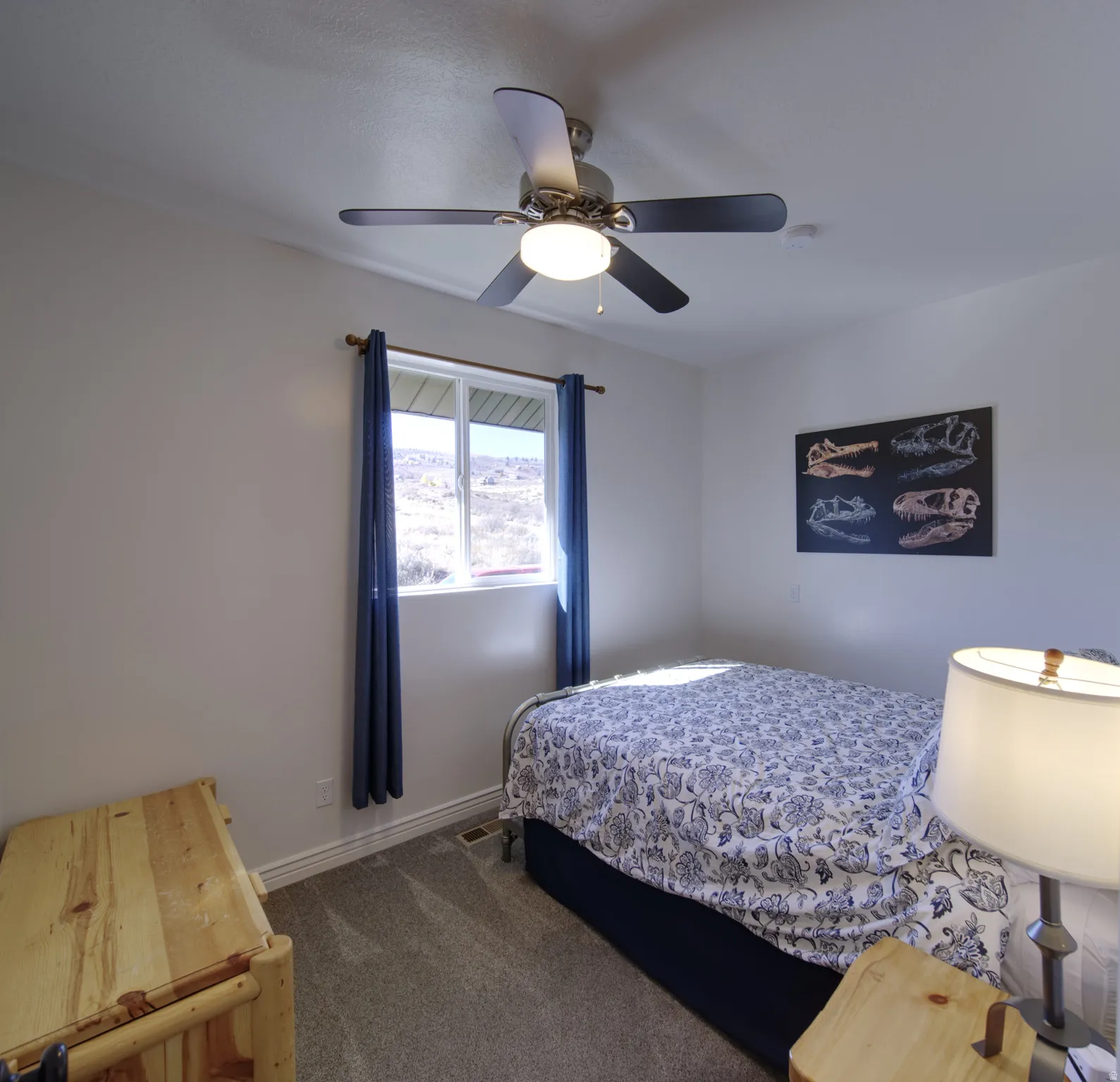 Bedroom featuring a ceiling fan with integrated lighting, carpeted flooring, and a window with blue curtain panels