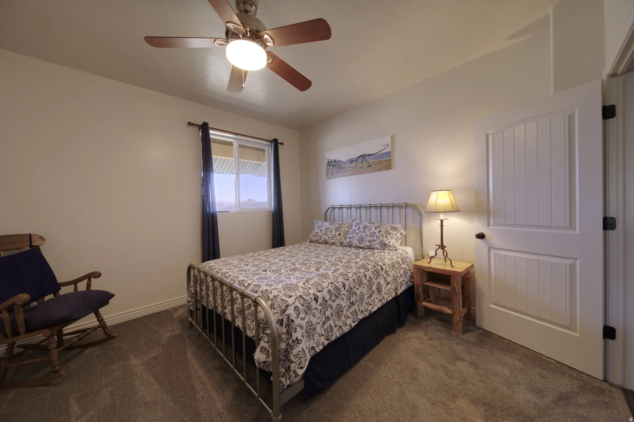 Carpeted bedroom featuring a ceiling fan with integrated lighting, a window with a valance, and a paneled interior door