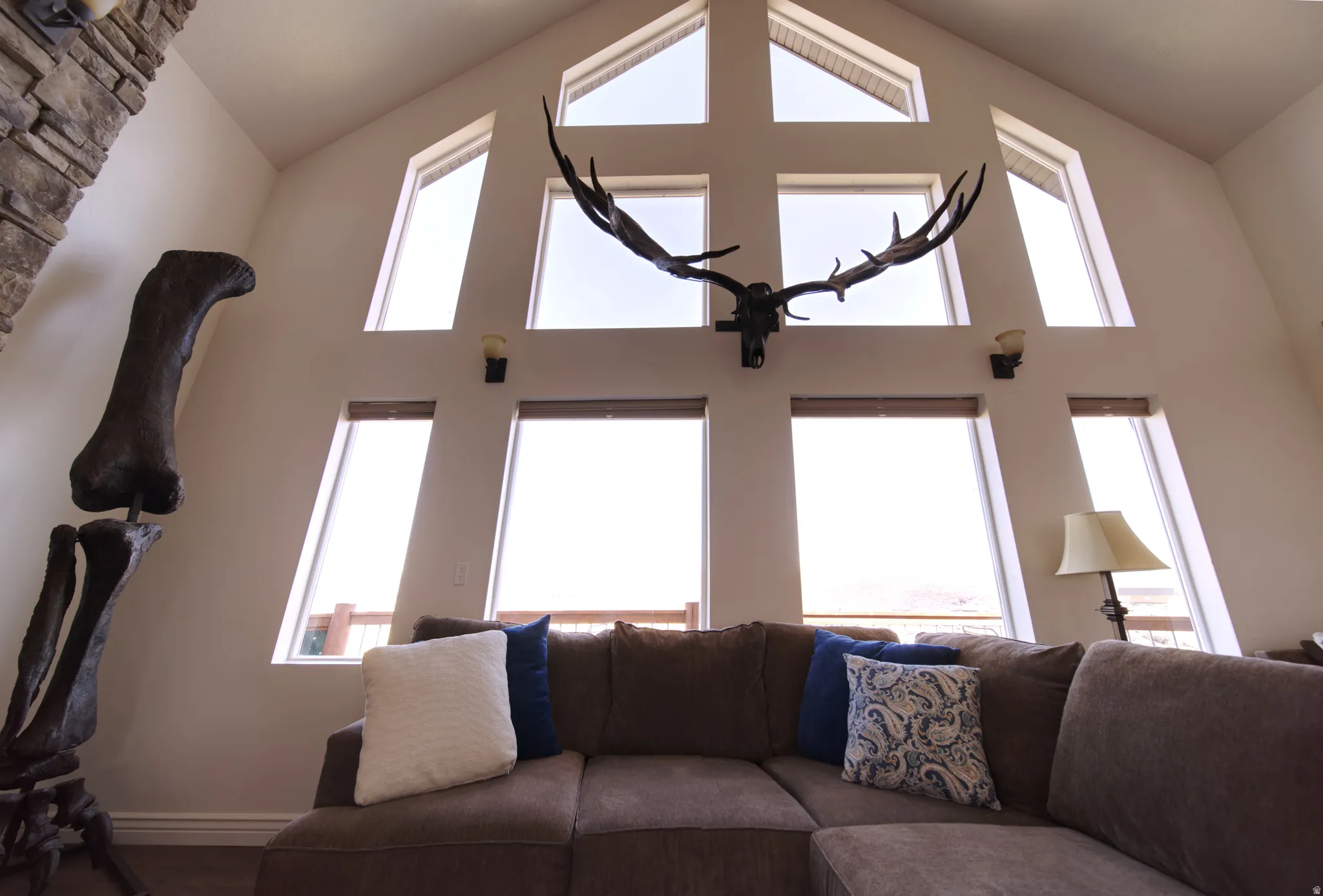 Vaulted ceilings featuring a large window array, stone-clad fireplace, and wall sconce lighting