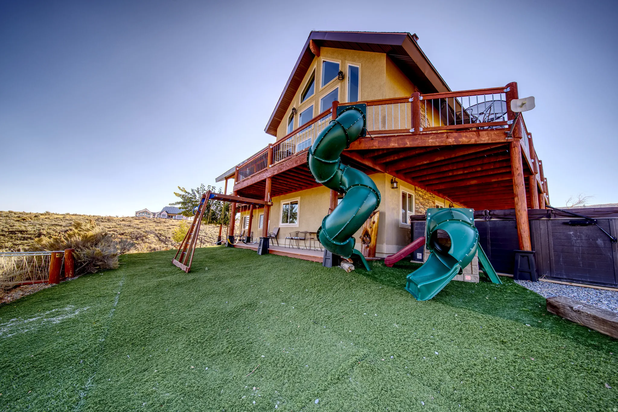 Terraced backyard featuring artificial turf, a two-story deck with wood railings, and a built-in slide from the upper deck to the yard