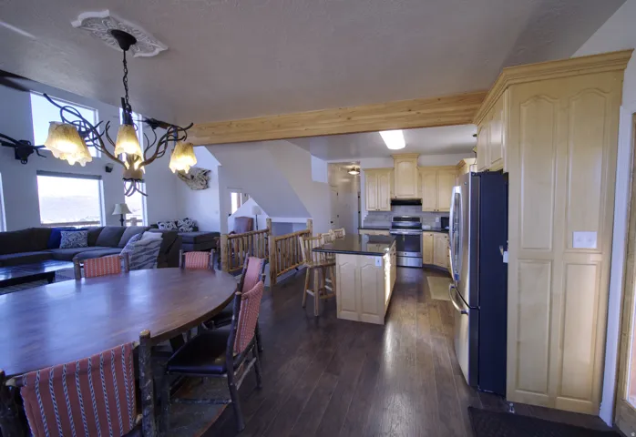 Open-concept living space with dark wood-finish flooring, a unique antler-design chandelier, and large windows