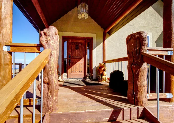Covered entry featuring natural wood posts, wood-finish decking, and a paneled entry door with decorative hardware