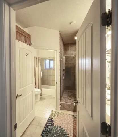 Bathroom featuring a walk-in shower with tile surround and stone-look floor, a separate tub/shower combination with tiled walls, and light-colored tile flooring