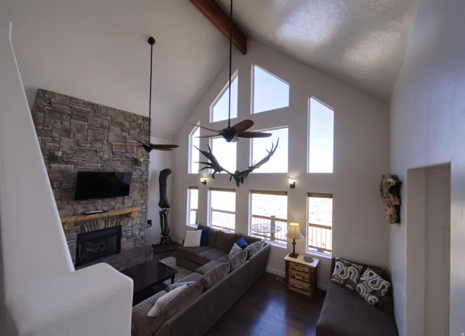 Vaulted ceiling with exposed wood beam, a stone fireplace with a wood mantel, and multiple large windows