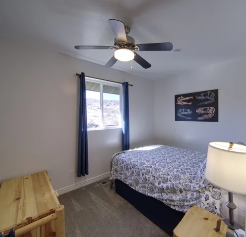 Bedroom featuring a ceiling fan with integrated lighting, carpeted flooring, and a window with blue curtain panels