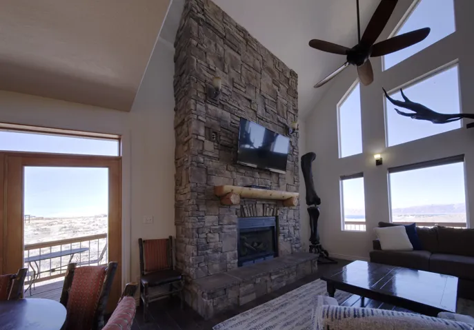 Vaulted living area featuring a floor-to-ceiling stone fireplace with a wood mantel, dark wood-finish flooring, and multiple large windows
