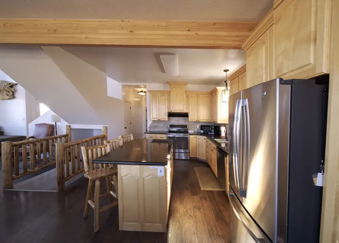 Kitchen featuring wood-finish flooring, light wood cabinetry, stainless steel appliances, and a central island with a dark countertop