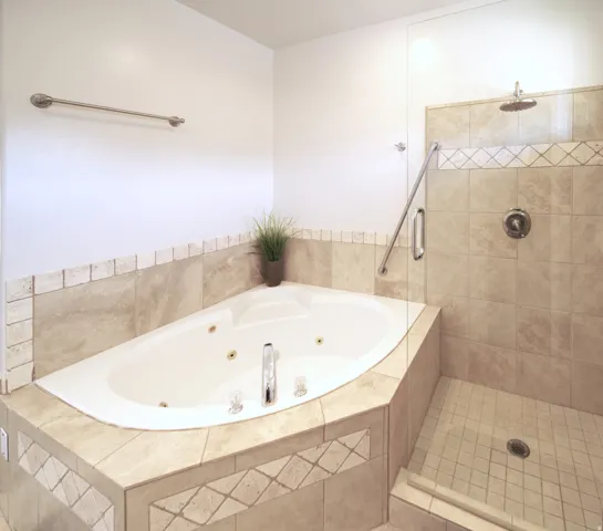 Corner jetted tub with tiled surround featuring decorative accents