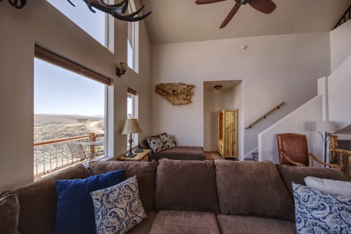Vaulted ceilings with a ceiling fan, a large window with roller shades, and a private balcony with metal railing