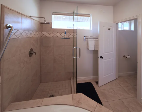 Tiled shower enclosure featuring a glass panel door and rain shower head