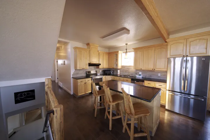 Spacious kitchen featuring wood-finish flooring, light wood cabinetry, dark countertops, and a full suite of stainless steel appliances