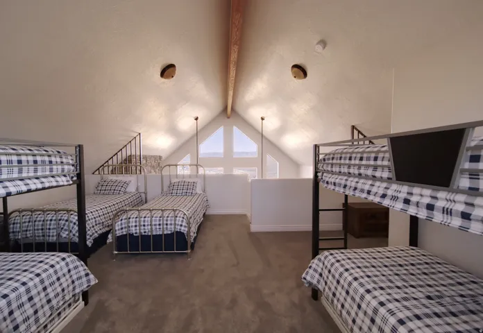 Upper-level living space featuring vaulted ceilings with a prominent exposed wood beam, large triangular windows providing natural illumination, and plush carpet flooring