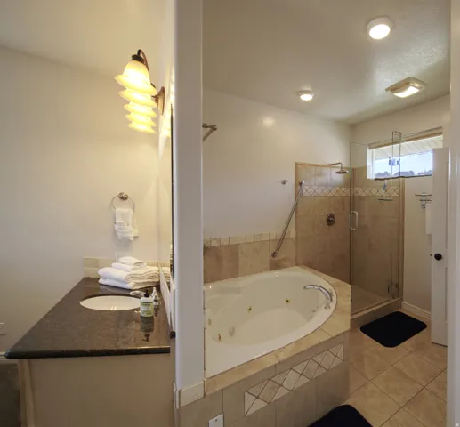 Bathroom featuring a jetted corner tub, a glass-enclosed shower with a rainfall showerhead, and a vanity with a dark countertop and undermount sink