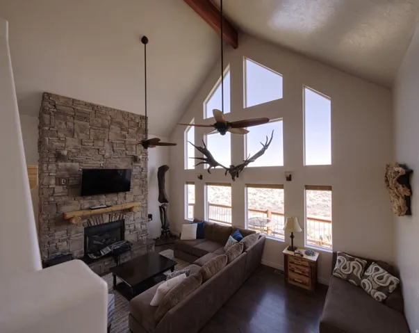 Vaulted ceiling great room featuring a stone-faced fireplace with a log mantel, integrated television, and a wood-finish ceiling fan