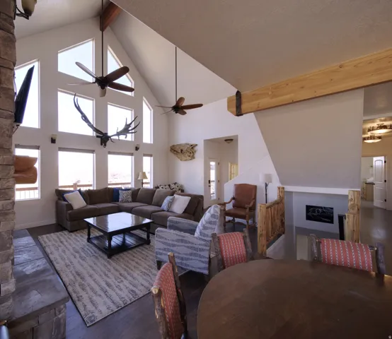 Living area featuring vaulted ceilings, a stone-clad fireplace, wood-finish flooring, a wall of windows, and exposed ceiling beams