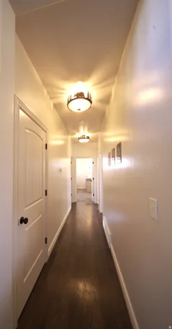Hallway featuring wood-finish flooring, white walls, and decorative flush-mount lighting fixtures