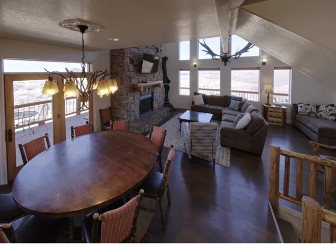 Open-concept living space featuring wood-finish flooring, a stone-clad fireplace, and multiple windows