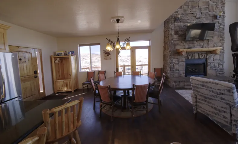 Open-concept living space featuring wood-finish flooring, a stone fireplace with a log mantel, and a dining area with direct exterior access