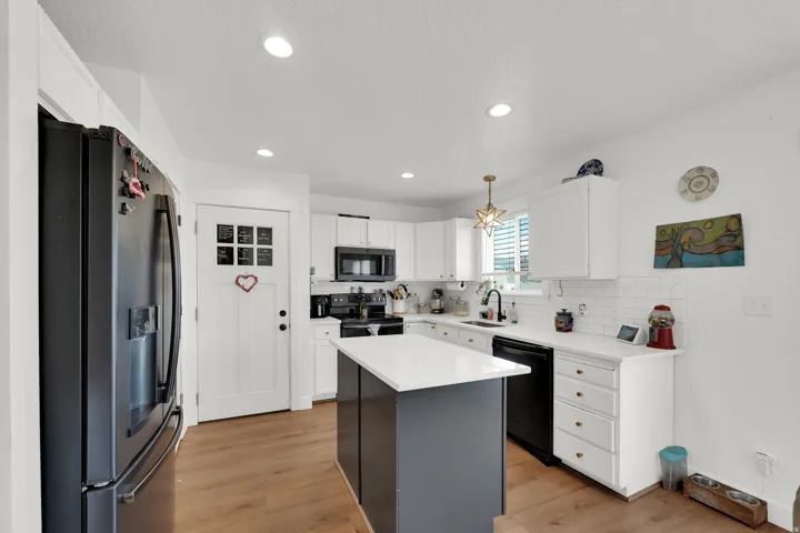 Modern kitchen featuring a central island with a light-colored countertop, white cabinetry, a black appliance suite, and wood-finish flooring