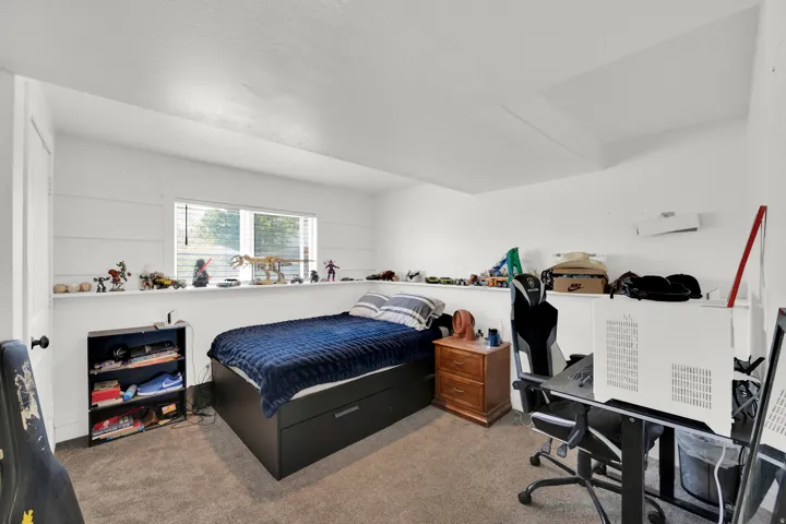 Carpeted room featuring a window with horizontal blinds, white walls, and a built-in wall shelf