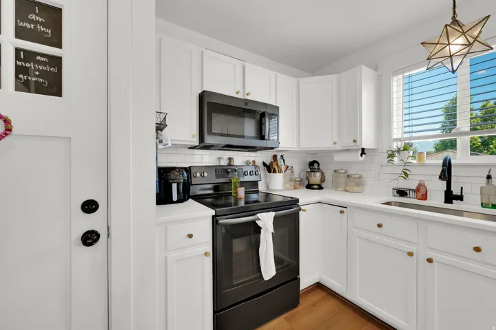 Modern kitchen featuring white cabinetry with brass hardware, a white subway tile backsplash, and a large window above the sink