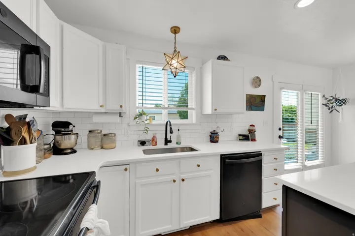 Kitchen featuring white cabinetry, white countertops, a subway tile backsplash, a black dishwasher, and wood-finish flooring