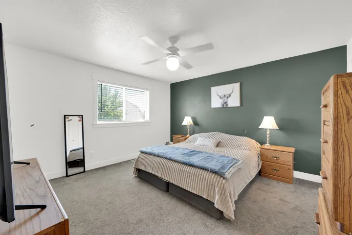 Spacious bedroom featuring neutral carpeting, a prominent accent wall, a ceiling fan with integrated lighting, and a single window with horizontal blinds