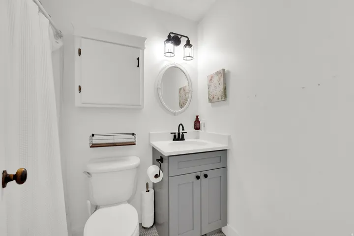Bathroom featuring a gray vanity with a white countertop and integrated sink, a wall-mounted medicine cabinet, an oval mirror, and a black-finish vanity light fixture