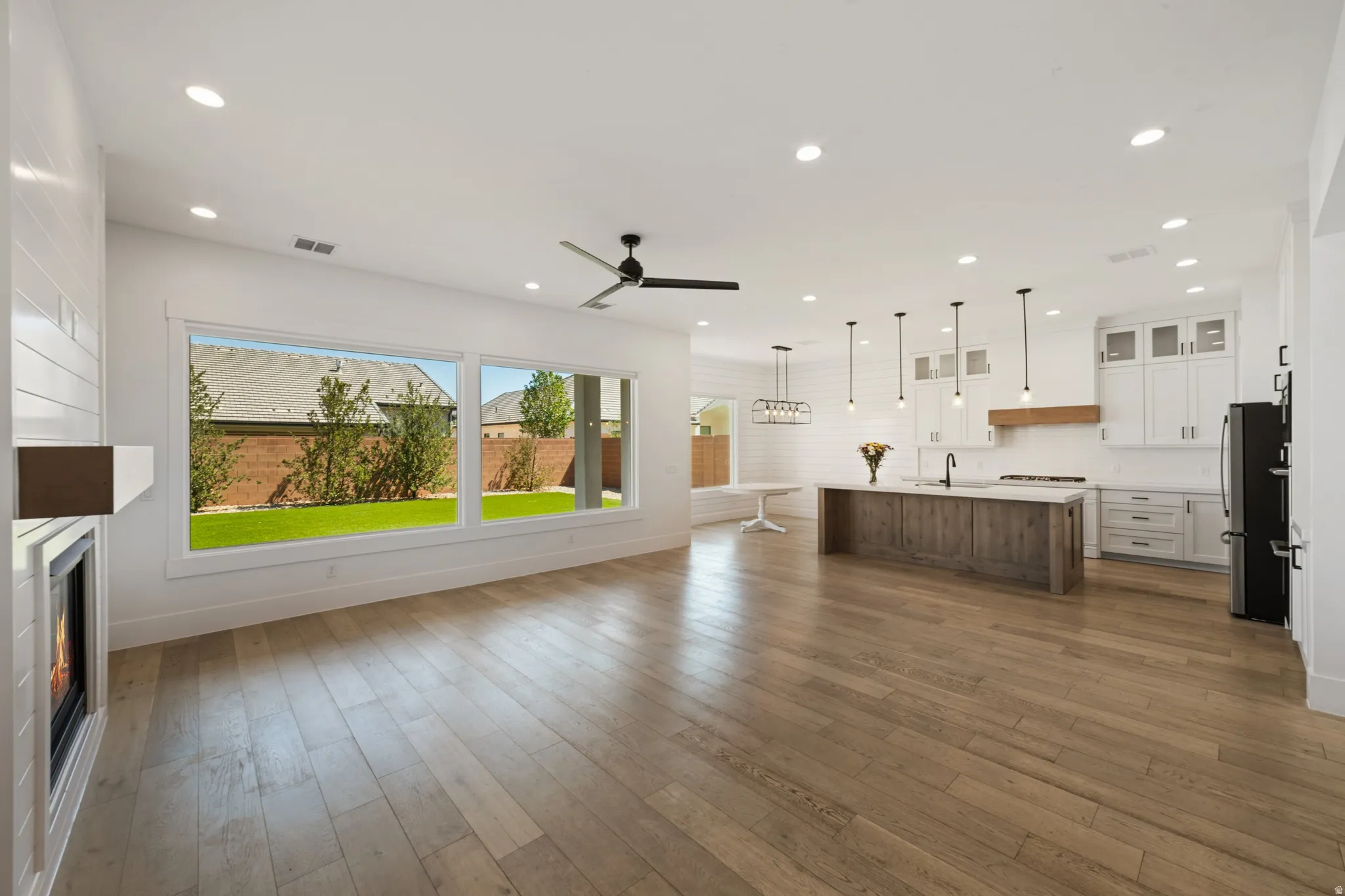 Open concept living area featuring wood-finish flooring, a linear fireplace with white shiplap surround, and a ceiling fan