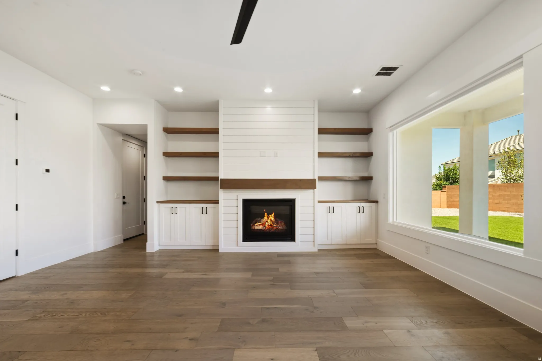 Living area featuring wood-finish flooring, a contemporary fireplace with a shiplap surround, integrated cabinetry, and open shelving