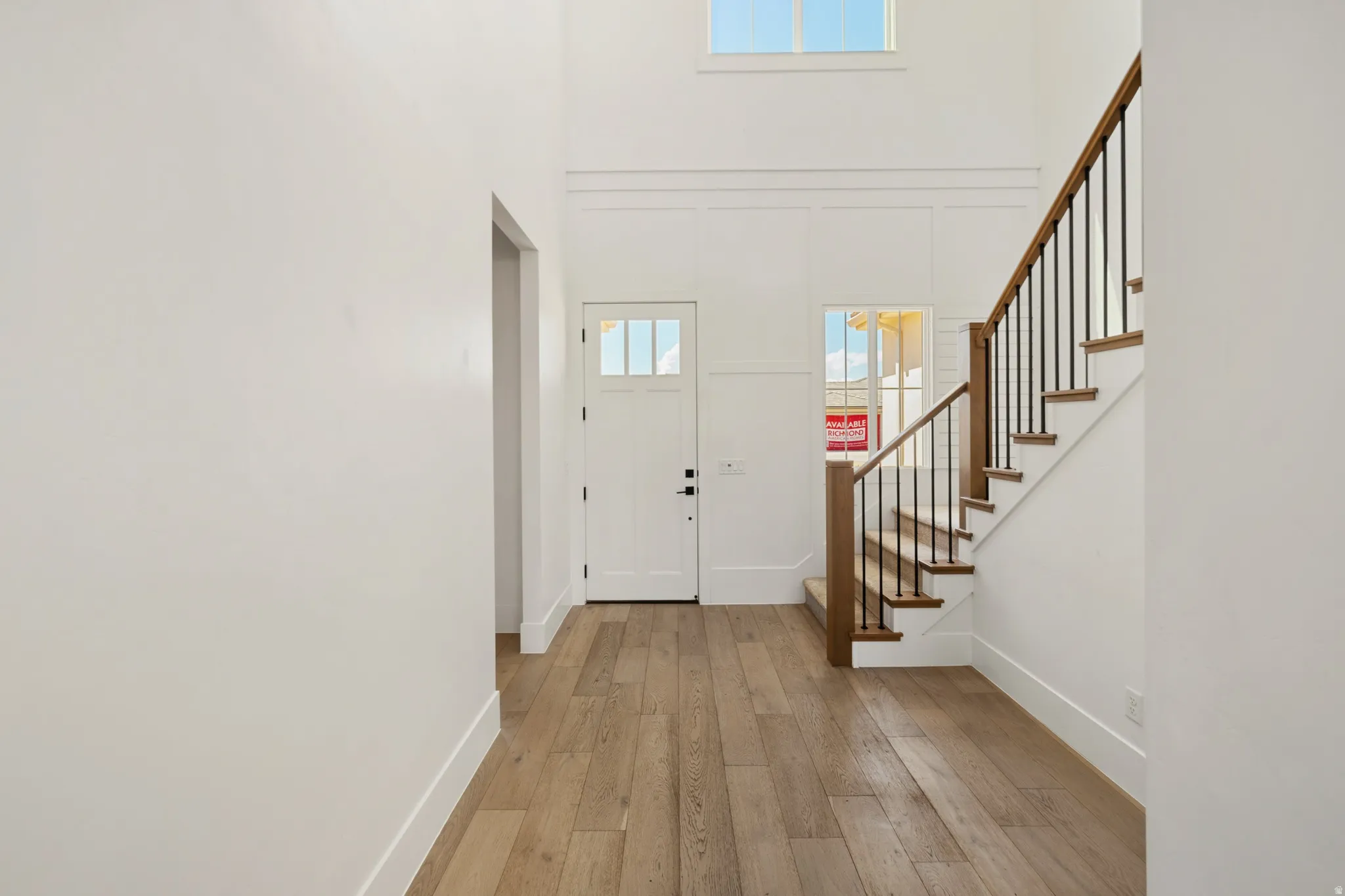 Foyer featuring wood-finish flooring, a two-story ceiling, a white paneled front door with lites, and a staircase with wood treads and a black metal spindle railing