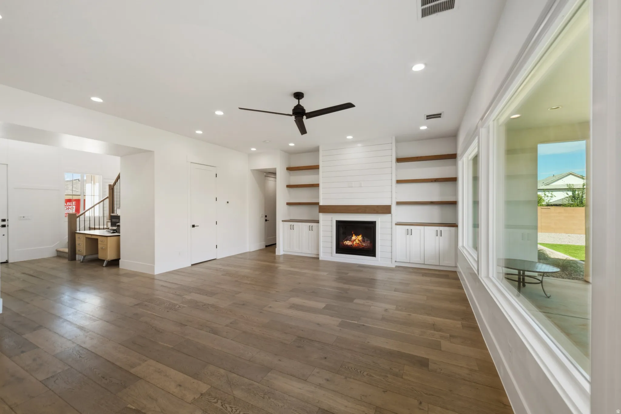 Spacious living area featuring wood-finish flooring, a shiplap fireplace with built-in shelving and cabinetry, recessed lighting, and large picture windows