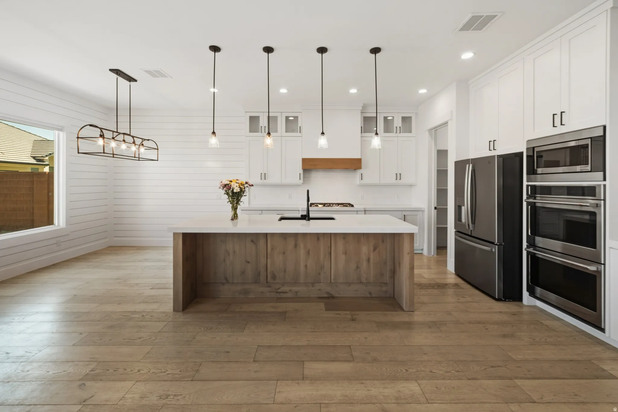 Open-concept kitchen featuring an oversized island with a light wood-finish base, contrasting white countertop, and pendant lighting
