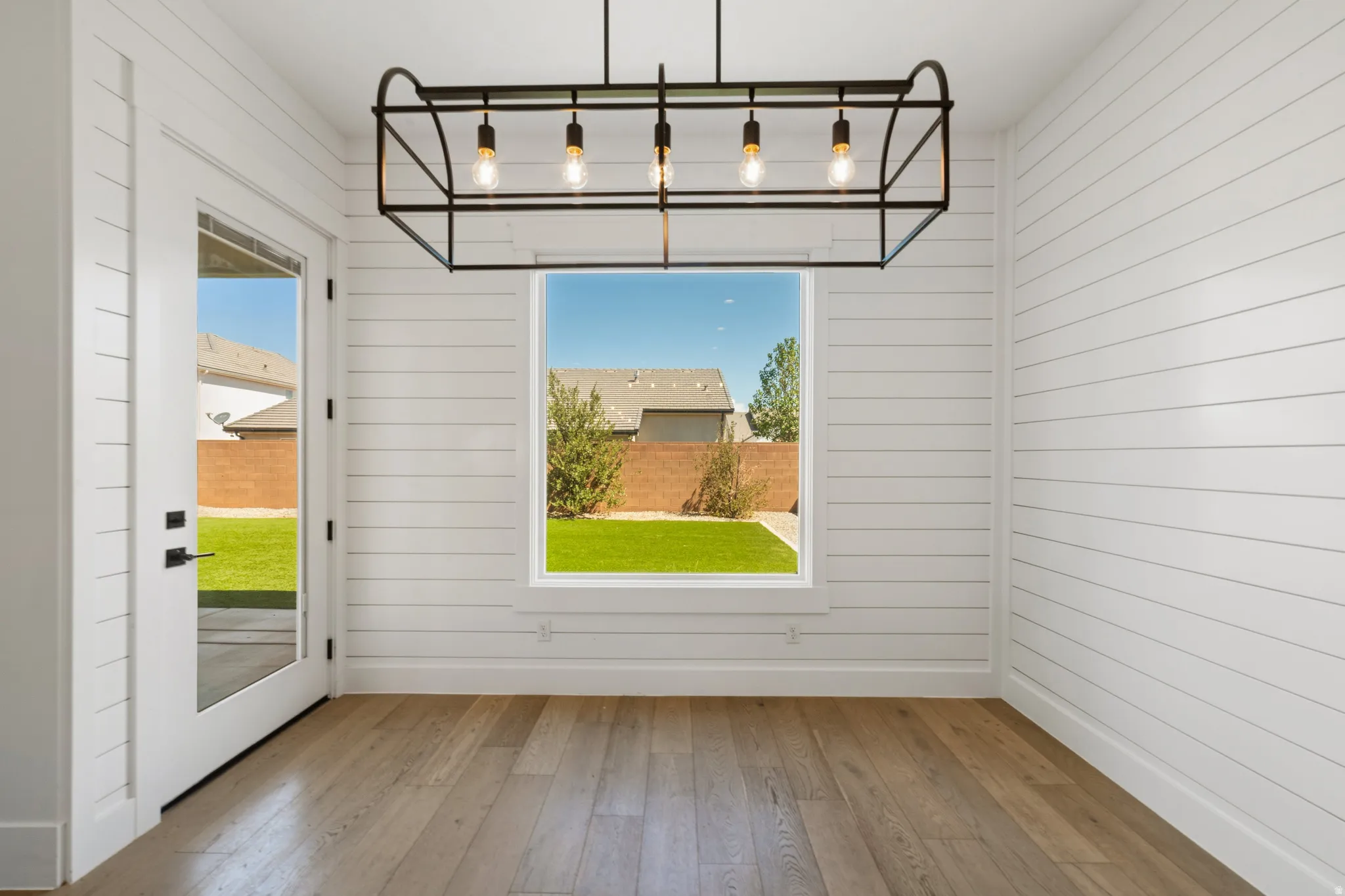 Interior space featuring shiplap walls, wood-finish flooring, a contemporary linear chandelier, a large window, and a glass-paned exterior door