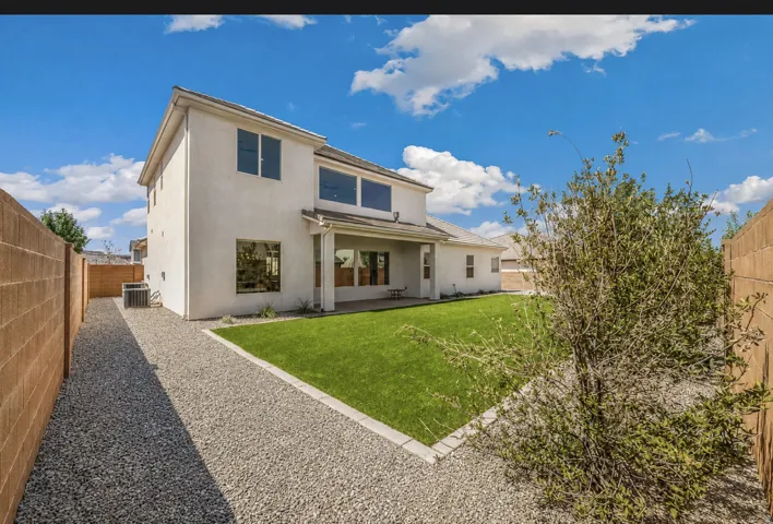 Stucco exterior with multiple windows, a covered patio, and a grass lawn