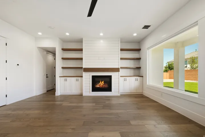 Living area featuring wood-finish flooring, a contemporary fireplace with a shiplap surround, integrated cabinetry, and open shelving
