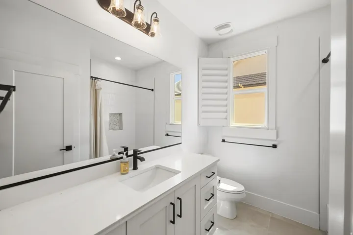 Modern bathroom featuring a single vanity with a white countertop and undermount sink, matte black hardware, and a large wall-mounted mirror