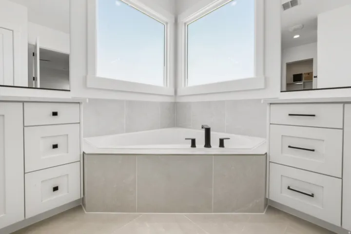 Corner soaking tub with a tiled surround, matte black fixtures, and two large windows