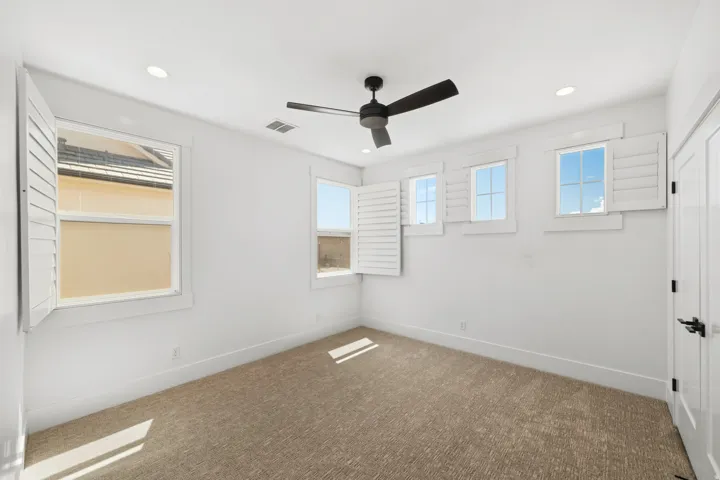 Bright room featuring white walls, textured carpeting, and a modern ceiling fan
