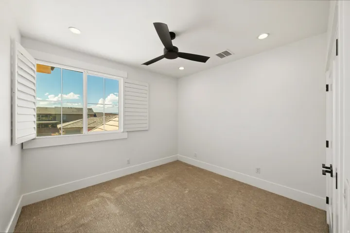 Bright interior space featuring a window with white louvered shutters, a ceiling fan, recessed lighting, and textured carpeting