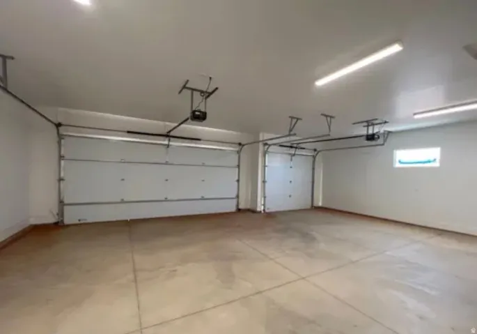 Spacious garage featuring two overhead doors with automatic openers, a concrete floor, bright overhead lighting, and a high window