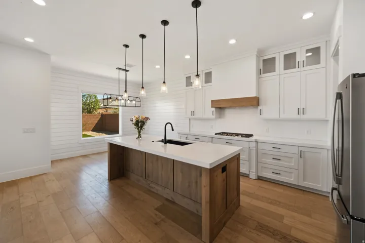 Contemporary kitchen featuring a large central island with a solid surface countertop and undermount sink, white shaker-style cabinetry with matte black hardware, a wood-finish range hood, and wood-finish flooring