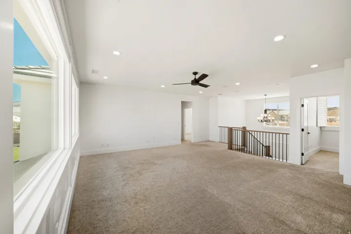 Spacious open area featuring neutral carpeting, recessed lighting, and a ceiling fan