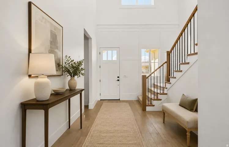 Bright entryway featuring wood-finish flooring and a staircase with natural wood handrails and black metal spindles
