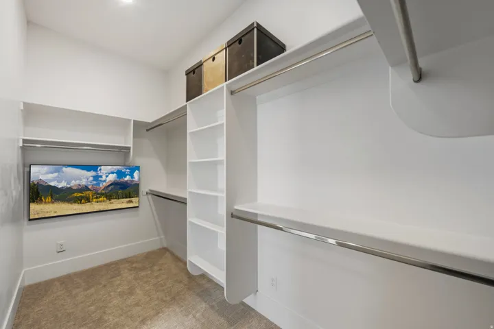 Walk-in closet featuring built-in white shelving, chrome hanging rods, recessed lighting, and soft carpet flooring