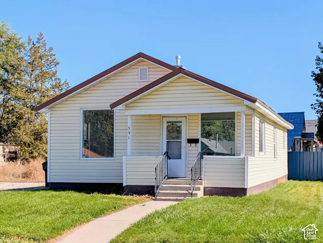 Exterior featuring light-toned horizontal siding, a gabled roofline, a covered front porch, and decorative wrought iron railings