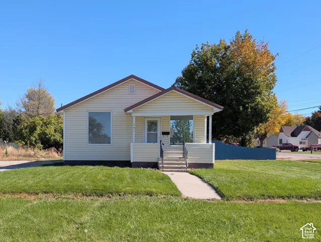 Single-story exterior featuring light-colored horizontal siding, a gabled roofline, a covered front porch with iron railings, and a concrete walkway