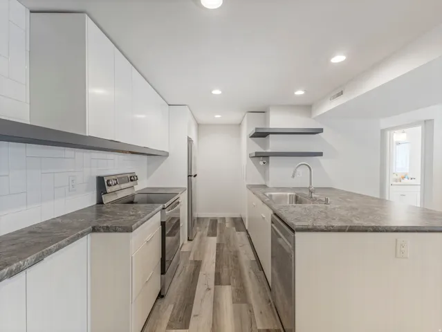 Modern kitchen featuring white flat-panel cabinetry, a stainless steel appliance suite, and wood-finish flooring