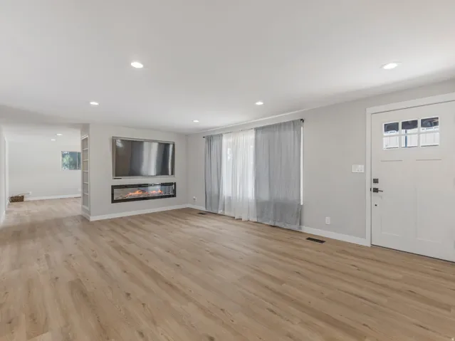 Open-concept living space featuring wood-finish flooring, recessed lighting, a modern built-in electric fireplace, and a multipaneled entry door