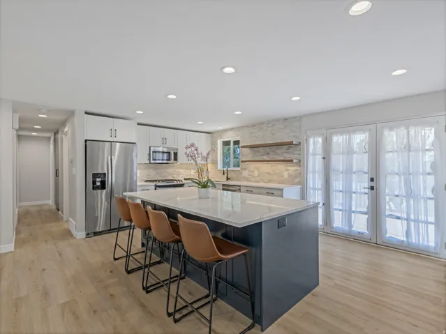 Modern kitchen featuring a large island with seating, stainless steel appliances, light wood-finish flooring, white cabinetry, and a light-toned tile backsplash